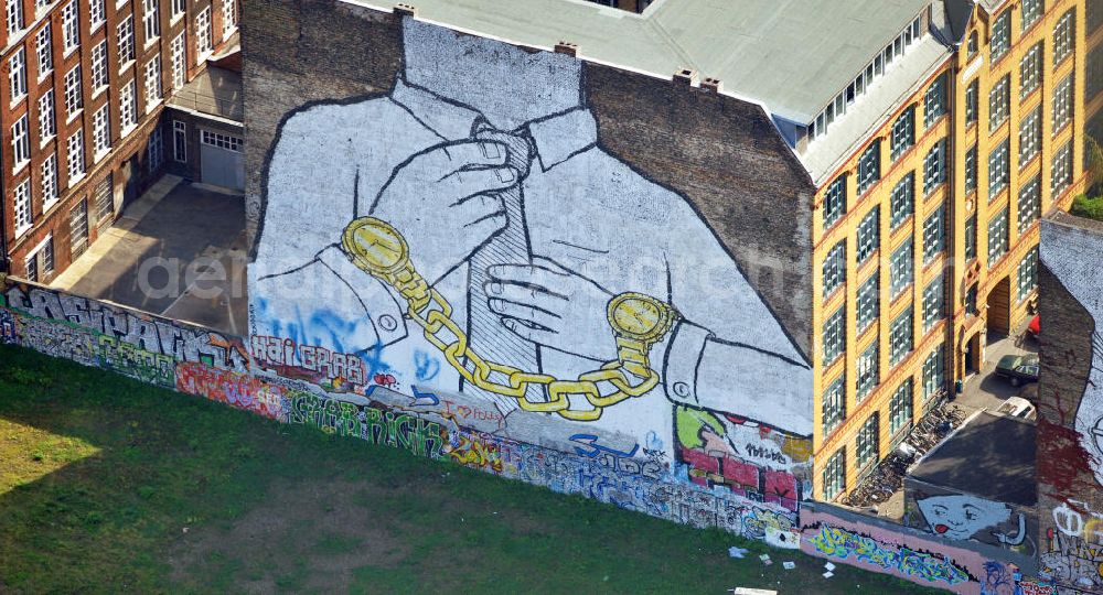 Berlin from the bird's eye view: Wandgemälde an der Cuvrystraße Ecke Schlesische Straße in Berlin-Kreuzberg des italienischen Street-Art-Künstlers Blu. Es zeigt einen kopflosen Krawattenträger mit golden Uhren als Handschellen. Mural painting in Berlin-Kreuzberg of the italien street art artist Blu.