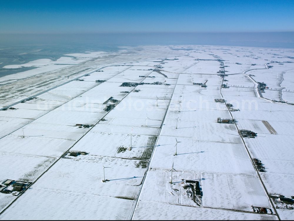 Aerial photograph Neufelderkoog - Wind power wheels and turbines in Neufelderkoog on the coast of the North Sea and the shores of the river Elbe. The turbines are placed between snowed and icy fields in winter. Overview of the agricultural structures as well as the wheels used to create energy