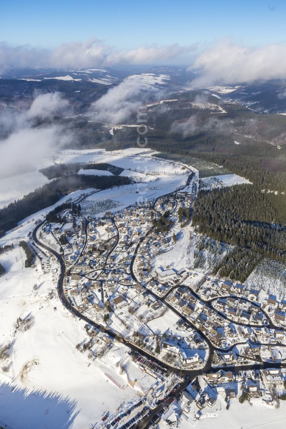 Altastenberg from above - View of the partially snow covered, foggy and cloudy winter landscape of Altastenberg in the state of North Rhine-Westphalia. At the outskirts of the village are located the ski - downhill and skiing trails