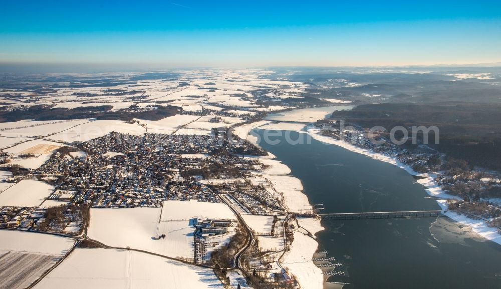 Möhnesee from the bird's eye view: Wintry snowy townscape with streets and houses of the residential areas in the district Koerbecke at the Moehne lake in Moehnesee in the state North Rhine-Westphalia