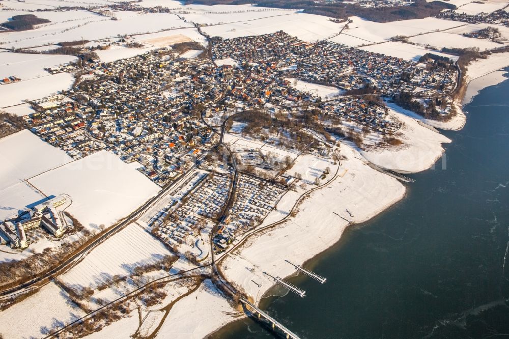 Möhnesee from the bird's eye view: Wintry snowy townscape with streets and houses of the residential areas in the district Koerbecke in Moehnesee in the state North Rhine-Westphalia