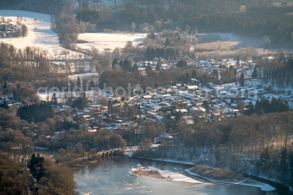 Aerial photograph Möhnesee - Wintry snowy townscape with streets and houses of the residential areas in the district Voellinghausen with the Warmeler bridge in Moehnesee in the state North Rhine-Westphalia