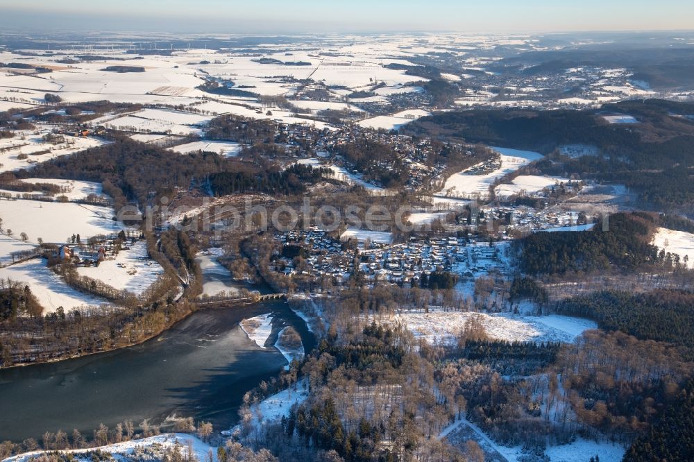 Möhnesee from the bird's eye view: Wintry snowy townscape with streets and houses of the residential areas in the district Voellinghausen with the Warmeler bridge in Moehnesee in the state North Rhine-Westphalia