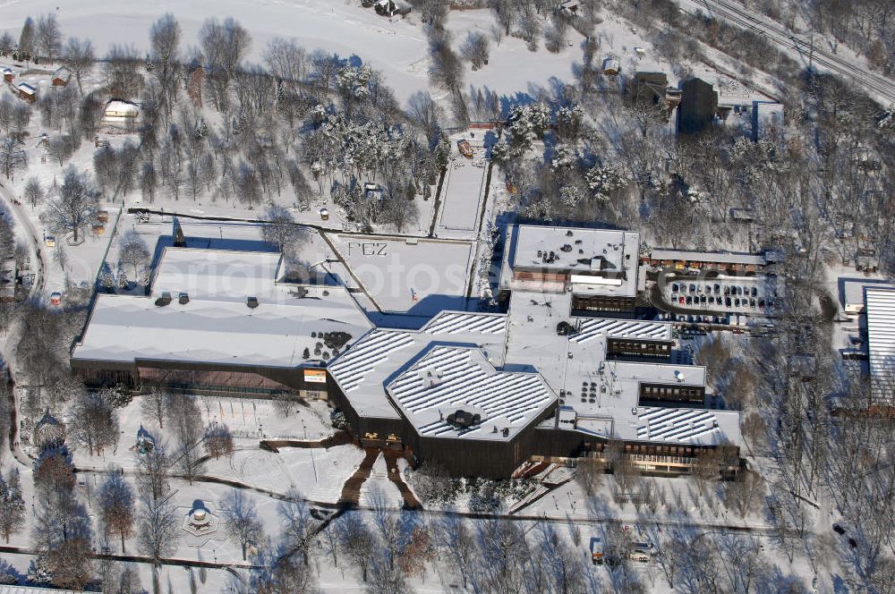 Berlin from the bird's eye view: Blick auf das winterlich, verschneite Freizeit- und Erholungszentrum (FEZ). Die 1951 im östlichen Bereich der Wuhlheide für die Jungen Pioniere erbaute „Pionierrepublik Ernst Thälmann“ (später: Pionierpark „Ernst Thälmann“) umfasst neben weiteren Attraktionen eine Freilichtbühne (heute Kindl-Bühne Wuhlheide) und die Parkeisenbahn Wuhlheide (Schmalspurbahn), die von Kindern und Jugendlichen (ursprünglich von Jungen Pionieren) betrieben wird, ein Stadion und einen Badesee. Die Pionierrepublik wurde zum ersten Deutschlandtreffen der Jugend und Studenten eröffnet. 1979, zum 30. Jahrestag der DDR, entstand das zentrale Pionierhaus, der Pionierpalast (Bauzeit: 1976–1979, Grundsteinlegung: 2. Juni 1976, Architekt: Günter Stahn, Material: u. a. Lärchenholz und Kalksandstein, Gesamtkosten: ca. 180 Mio. Mark), der auf einer Fläche von 13.000 Quadratmetern Veranstaltungsräume, Räume für Arbeitsgemeinschaften (z. B. eine Computer-AG), ein Restaurant, eine Sporthalle und ein Schwimmbad mit 50-Meter-Bahn umfasst. Spektakulärer Höhepunkt war ein „Kosmonautentrainingszentrum“. Gleichzeitig entstand auch ein großer Kinderspielplatz. Der Pionierpalast war damit eine der größten Anlagen dieser Art in der DDR.