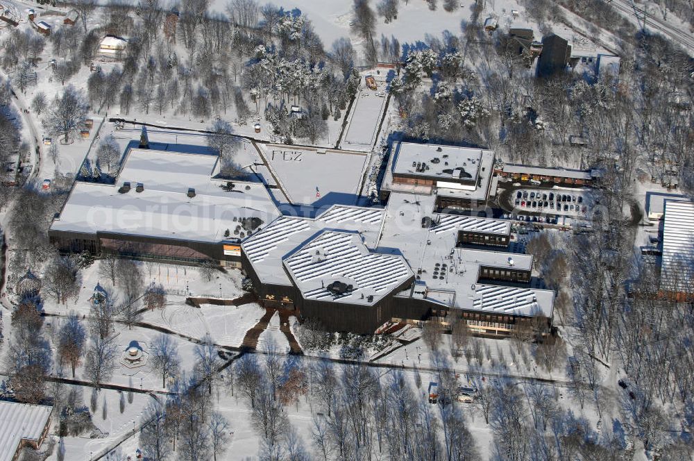 Aerial image Berlin - Blick auf das winterlich, verschneite Freizeit- und Erholungszentrum (FEZ). Die 1951 im östlichen Bereich der Wuhlheide für die Jungen Pioniere erbaute „Pionierrepublik Ernst Thälmann“ (später: Pionierpark „Ernst Thälmann“) umfasst neben weiteren Attraktionen eine Freilichtbühne (heute Kindl-Bühne Wuhlheide) und die Parkeisenbahn Wuhlheide (Schmalspurbahn), die von Kindern und Jugendlichen (ursprünglich von Jungen Pionieren) betrieben wird, ein Stadion und einen Badesee. Die Pionierrepublik wurde zum ersten Deutschlandtreffen der Jugend und Studenten eröffnet. 1979, zum 30. Jahrestag der DDR, entstand das zentrale Pionierhaus, der Pionierpalast (Bauzeit: 1976–1979, Grundsteinlegung: 2. Juni 1976, Architekt: Günter Stahn, Material: u. a. Lärchenholz und Kalksandstein, Gesamtkosten: ca. 180 Mio. Mark), der auf einer Fläche von 13.000 Quadratmetern Veranstaltungsräume, Räume für Arbeitsgemeinschaften (z. B. eine Computer-AG), ein Restaurant, eine Sporthalle und ein Schwimmbad mit 50-Meter-Bahn umfasst. Spektakulärer Höhepunkt war ein „Kosmonautentrainingszentrum“. Gleichzeitig entstand auch ein großer Kinderspielplatz. Der Pionierpalast war damit eine der größten Anlagen dieser Art in der DDR.