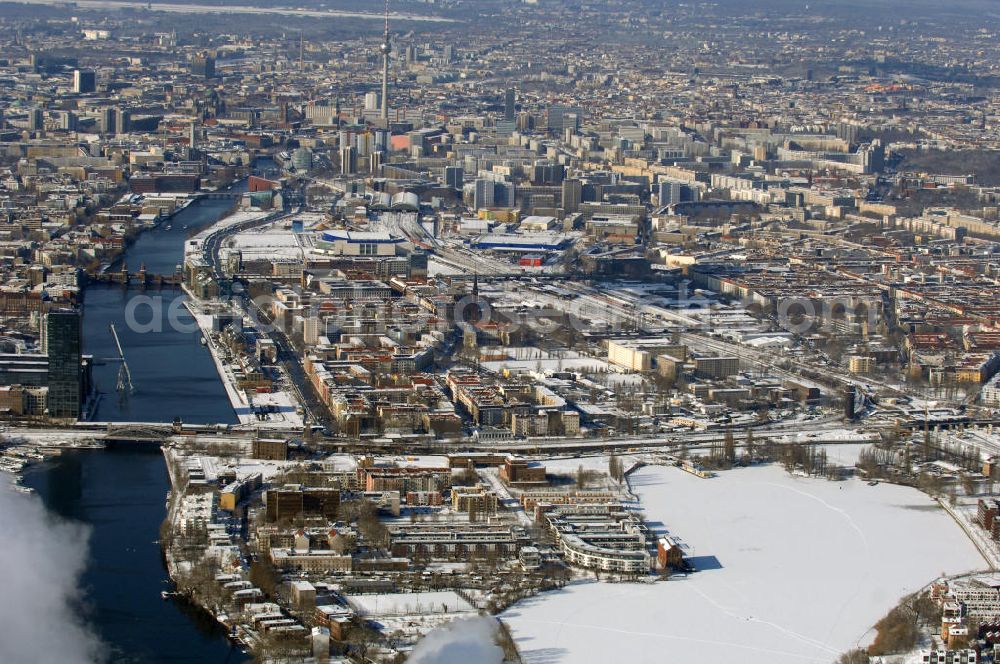 Berlin from above - Winterlich, verschneite Stadtansicht Berlins vom Bereich des Berliner Osthafens mit der dahinter liegenden O2 Arena im Friedrichshain und auf der kinken Spreeseite das Areal des Treptowers der ALLIANZ und Wohngebiete in Kreuzberg. Im Hintergrund das Berliner Stadtzentrum mit dem Berliner Fernsehturm