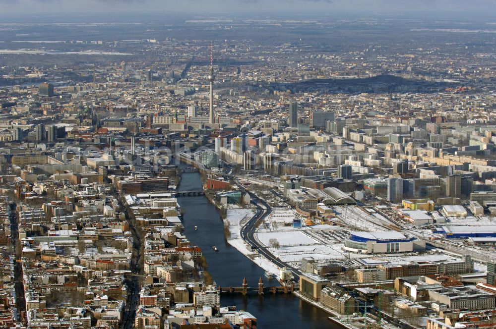 Aerial image Berlin - Winterlich, verschneite Stadtansicht Berlins vom Bereich des Berliner Osthafens mit der dahinter liegenden O2 Arena im Friedrichshain und auf der kinken Spreeseite das Areal des Treptowers der ALLIANZ und Wohngebiete in Kreuzberg. Im Hintergrund das Berliner Stadtzentrum mit dem Berliner Fernsehturm