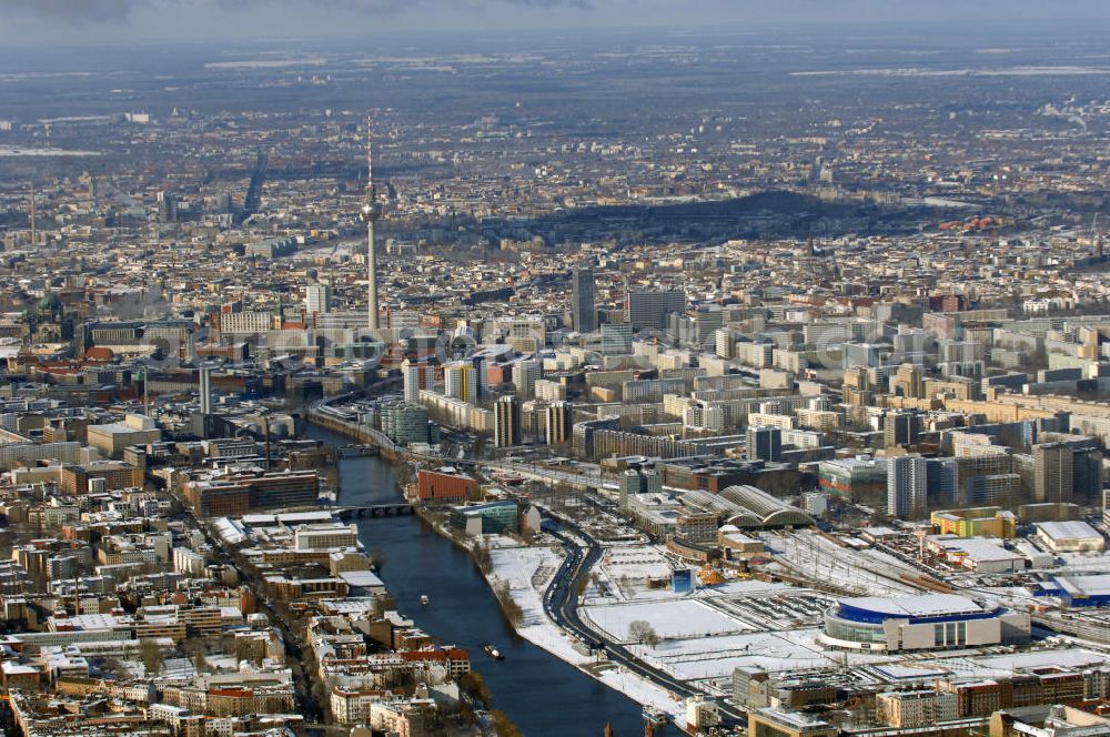 Aerial image Berlin - Winterlich, verschneite Stadtansicht Berlins vom Bereich des Berliner Osthafens mit der dahinter liegenden O2 Arena im Friedrichshain und auf der kinken Spreeseite das Areal des Treptowers der ALLIANZ und Wohngebiete in Kreuzberg. Im Hintergrund das Berliner Stadtzentrum mit dem Berliner Fernsehturm