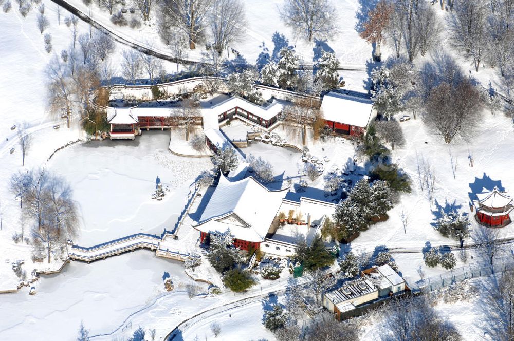 Berlin from above - Blick auf den winterlich verschneiten Chinesischen Garten im Erholungspark Marzahn. Der Erholungspark Marzahn liegt im Berliner Bezirk Marzahn-Hellersdorf am nördlichen Fuß des Kienbergs und wurde am 9. Mai 1987 anlässlich der 750-Jahr-Feier von Berlin als Berliner Gartenschau und Geschenk der Gärtner an die Hauptstadt der DDR (Ost-Berlin) eröffnet und sollte somit ein Gegenstück zum Britzer Garten im damaligen West-Berlin darstellen. 1991 wurde die Berliner Gartenschau nicht nur in Erholungspark Marzahn umbenannt, sondern auch umgebaut: Große Spiel- und Liegewiesen sowie neue Spielplätze entstanden, Bäume wurden gepflanzt und Sondergärten überarbeitet und erweitert. Der neu gestaltete Park sollte den 300.000 Bewohnern der umliegenden Großsiedlungen als vielfältig nutzbare Erholungslandschaft dienen. Seit Oktober 2000 ist diese durch ihre Gärten der Welt auch weit über die Stadtgrenzen hinaus bekannt. 2005 wurde der Chinesische Garten im Erholungspark Marzahn als drittschönste Parkanlage Deutschlands ausgezeichnet. Außerdem gehört der Erholungspark zu den 365 Orten im Land der Ideen.