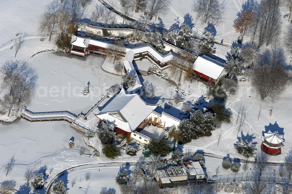 Aerial image Berlin - Blick auf den winterlich verschneiten Chinesischen Garten im Erholungspark Marzahn. Der Erholungspark Marzahn liegt im Berliner Bezirk Marzahn-Hellersdorf am nördlichen Fuß des Kienbergs und wurde am 9. Mai 1987 anlässlich der 750-Jahr-Feier von Berlin als Berliner Gartenschau und Geschenk der Gärtner an die Hauptstadt der DDR (Ost-Berlin) eröffnet und sollte somit ein Gegenstück zum Britzer Garten im damaligen West-Berlin darstellen. 1991 wurde die Berliner Gartenschau nicht nur in Erholungspark Marzahn umbenannt, sondern auch umgebaut: Große Spiel- und Liegewiesen sowie neue Spielplätze entstanden, Bäume wurden gepflanzt und Sondergärten überarbeitet und erweitert. Der neu gestaltete Park sollte den 300.000 Bewohnern der umliegenden Großsiedlungen als vielfältig nutzbare Erholungslandschaft dienen. Seit Oktober 2000 ist diese durch ihre Gärten der Welt auch weit über die Stadtgrenzen hinaus bekannt. 2005 wurde der Chinesische Garten im Erholungspark Marzahn als drittschönste Parkanlage Deutschlands ausgezeichnet. Außerdem gehört der Erholungspark zu den 365 Orten im Land der Ideen.