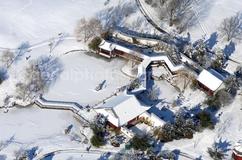 Aerial image Berlin - Blick auf den winterlich verschneiten Chinesischen Garten im Erholungspark Marzahn. Der Erholungspark Marzahn liegt im Berliner Bezirk Marzahn-Hellersdorf am nördlichen Fuß des Kienbergs und wurde am 9. Mai 1987 anlässlich der 750-Jahr-Feier von Berlin als Berliner Gartenschau und Geschenk der Gärtner an die Hauptstadt der DDR (Ost-Berlin) eröffnet und sollte somit ein Gegenstück zum Britzer Garten im damaligen West-Berlin darstellen. 1991 wurde die Berliner Gartenschau nicht nur in Erholungspark Marzahn umbenannt, sondern auch umgebaut: Große Spiel- und Liegewiesen sowie neue Spielplätze entstanden, Bäume wurden gepflanzt und Sondergärten überarbeitet und erweitert. Der neu gestaltete Park sollte den 300.000 Bewohnern der umliegenden Großsiedlungen als vielfältig nutzbare Erholungslandschaft dienen. Seit Oktober 2000 ist diese durch ihre Gärten der Welt auch weit über die Stadtgrenzen hinaus bekannt. 2005 wurde der Chinesische Garten im Erholungspark Marzahn als drittschönste Parkanlage Deutschlands ausgezeichnet. Außerdem gehört der Erholungspark zu den 365 Orten im Land der Ideen.