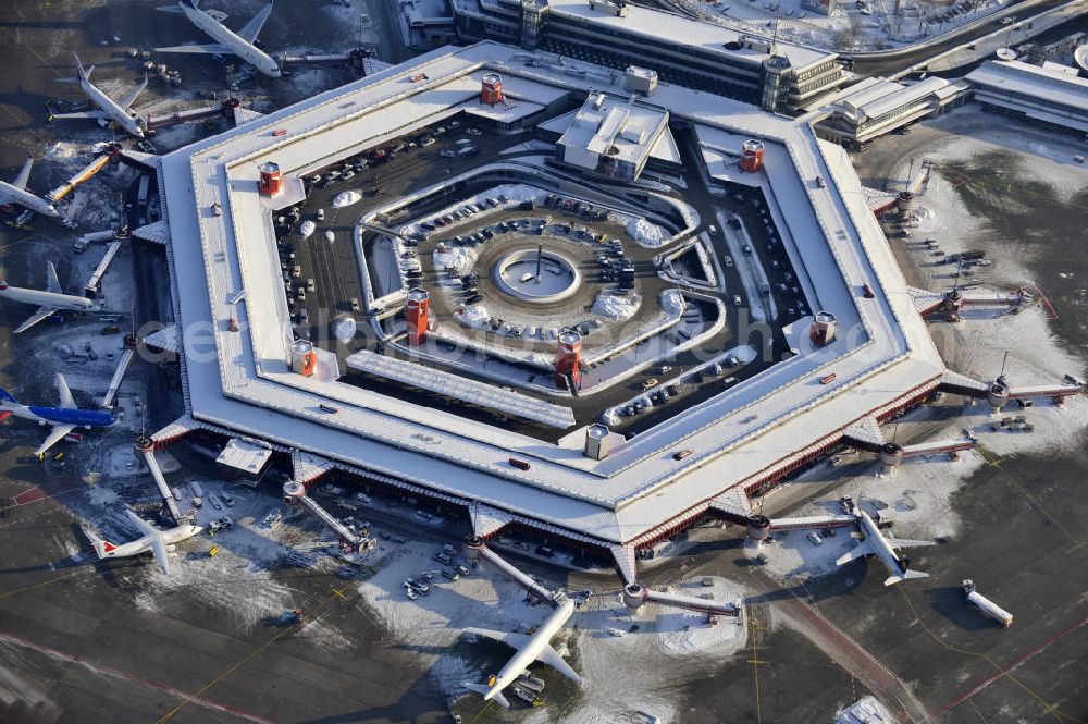 Aerial photograph Berlin - Winterlich verschneiter Blick auf Areal des Flughafen Berlin- Tegel. Am Abfertigungsterminal stehen Flugzeuge der DELTA , AIR Berlin und BRITISH AIRWAYS. View of the area of the airport Berlin-Tegel with the two runways. On the Terminal stand aircraft - operated by DELTA, AIR BERLIN and BRITISH AIRWAYS.